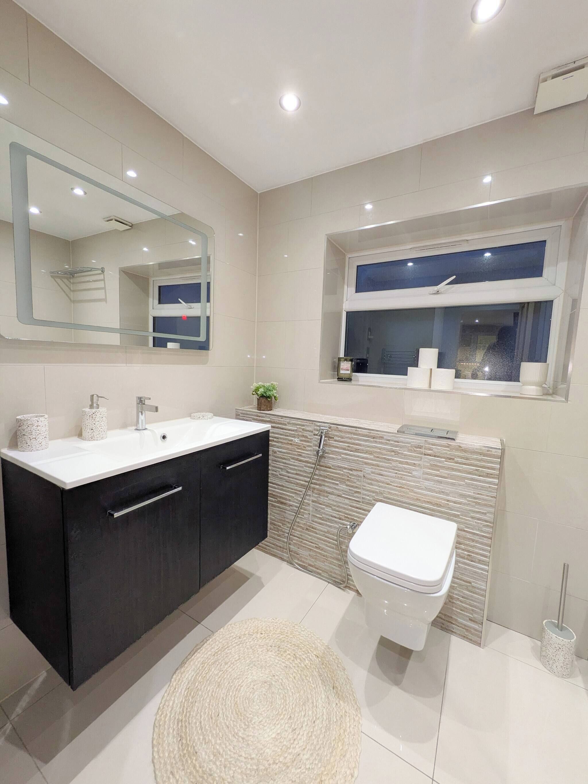 A modern bathroom with a large mirror, a sink, a toilet, and a shower area.