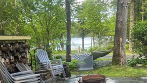 Eine Terrasse mit Adirondack-Stühlen, einer Feuerstelle und einem Holzstoß.