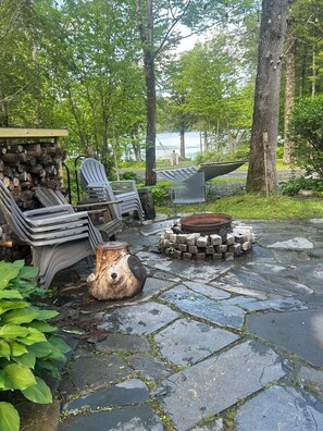 Eine Terrasse mit Adirondack-Stühlen, einer Feuerstelle und einem Holzstoß.