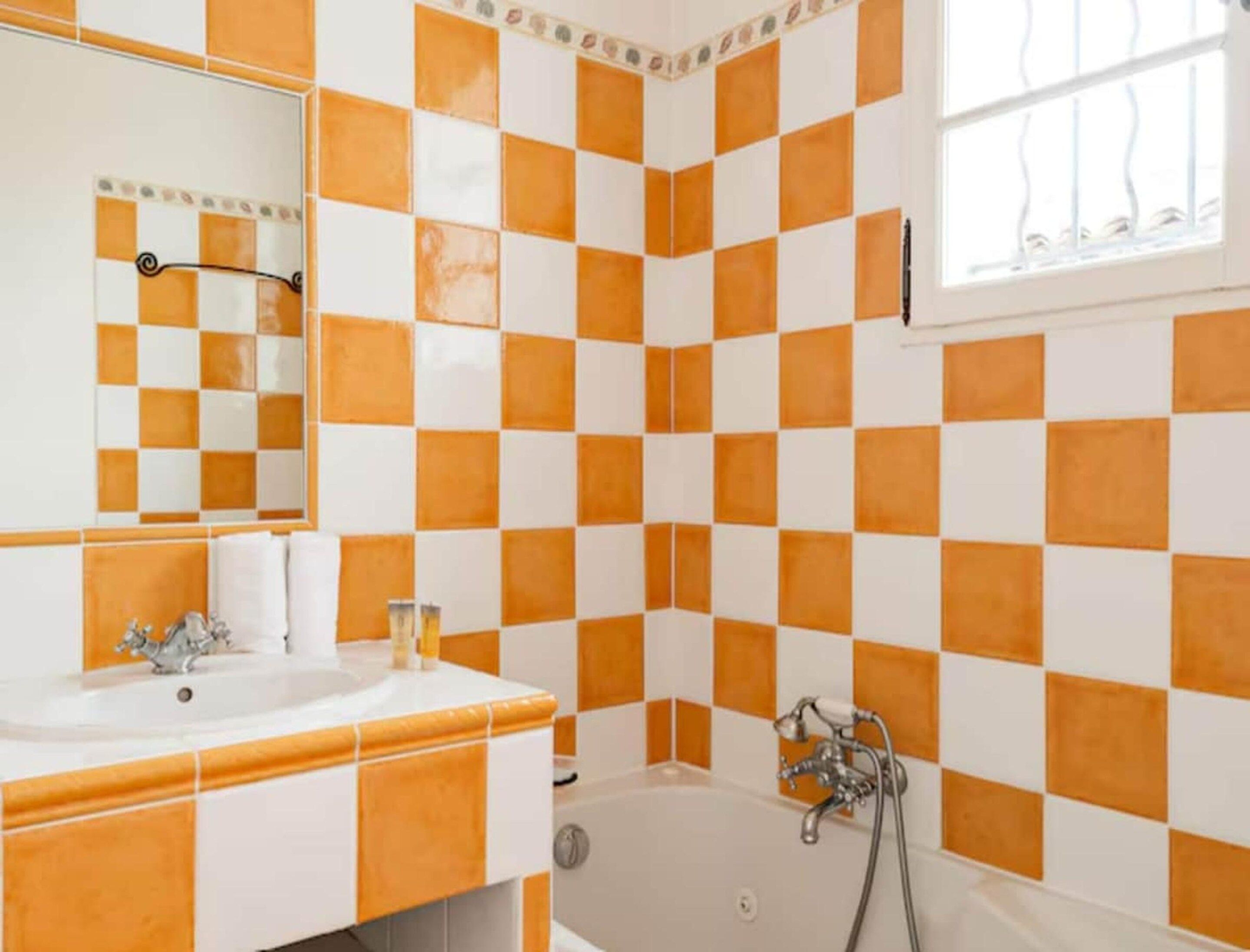 Une salle de bain avec un carrelage à motifs à carreaux, un lavabo, un miroir et une baignoire.
