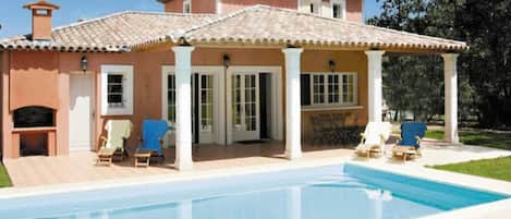 A two-story house with a swimming pool, outdoor seating, and a covered patio area.