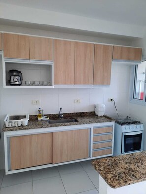 Eine kleine Küche mit Holzausbau, einer Arbeitsplatte aus Granit, einem eingebauten Herd und einer Kaffeemaschine.