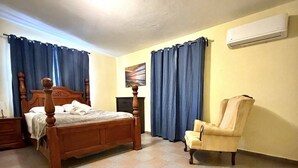 Quarto com cama de madeira, uma cadeira, mesa de cabeceira e ar condicionado na parede.
