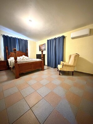 Een slaapkamer met een houten bed, een stoel, een nachtkastje en een airconditioner aan de muur.
