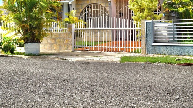 Uma casa de dois andares com telhado de telhas vermelhas, cerca branca e portão.