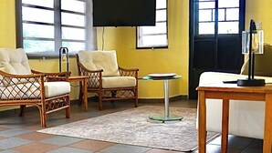 Quarto com ventilador no teto, duas cadeiras de vime, uma mesa redonda pequena, televisão de tela plana e janela com vista.
