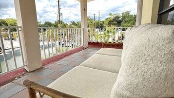 A covered outdoor seating area with a wooden chair, a white cushioned sofa, and a metal railing.