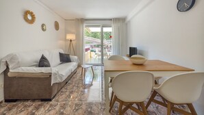 A modern living room with a sofa, dining table, chairs, and a view through a glass door to an outdoor area. - SunAndBed Zaragoza – Stylish Apartment with Terrace in Central Salou (Salou)
