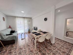 A compact living space with a dining area, a sofa, a TV, and a clock on the wall.