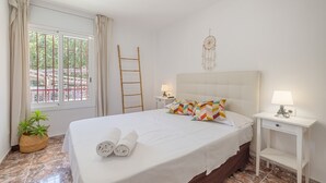 A bedroom with a bed, two bedside tables, a nightstand, a dreamcatcher, a window with curtains, a potted plant, and a wooden ladder. - SunAndBed Zaragoza – Stylish Apartment with Terrace in Central Salou (Salou)