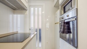 A narrow kitchen with a black countertop, a stainless steel oven, and a door with frosted glass panels. - SunAndBed Zaragoza – Stylish Apartment with Terrace in Central Salou (Salou)