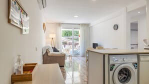 A compact living space with a sofa, a small table, a washing machine, and a view of the outdoors. - SunAndBed Zaragoza – Stylish Apartment with Terrace in Central Salou (Salou)