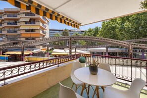 Uma varanda com vista para a paisagem urbana, incluindo um edifício com várias andares e varandas, e uma rua com lojas.