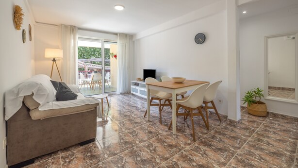 A modern living room with a sofa, a dining table with chairs, a TV, and a potted plant. - SunAndBed Zaragoza – Stylish Apartment with Terrace in Central Salou (Salou)