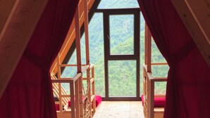 A wooden room with a bed, a window, and a view of a forest. - HAVALI BUNGALOWS (Camlihemsin)