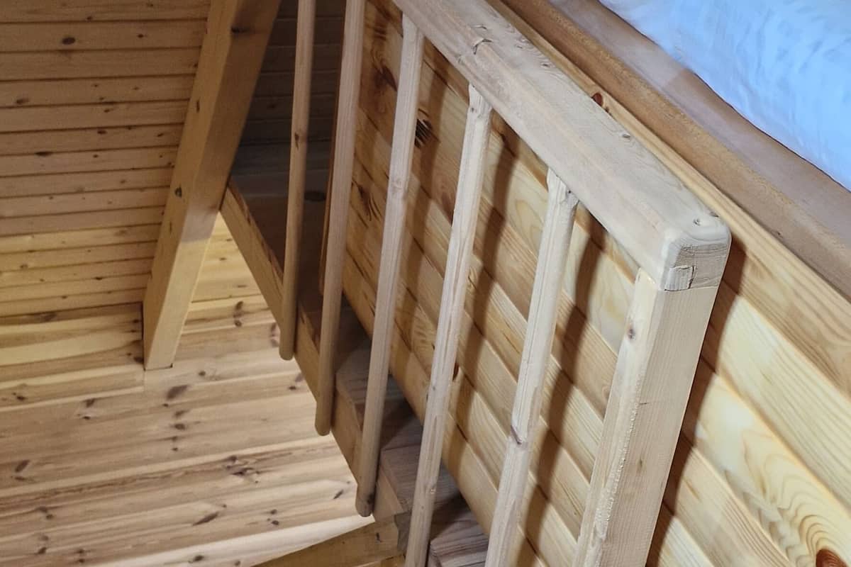 A wooden staircase leading to a bunk bed with a blue pillow.