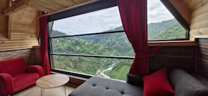 A room with a large window, a red sofa, a grey sofa, and a small round table.