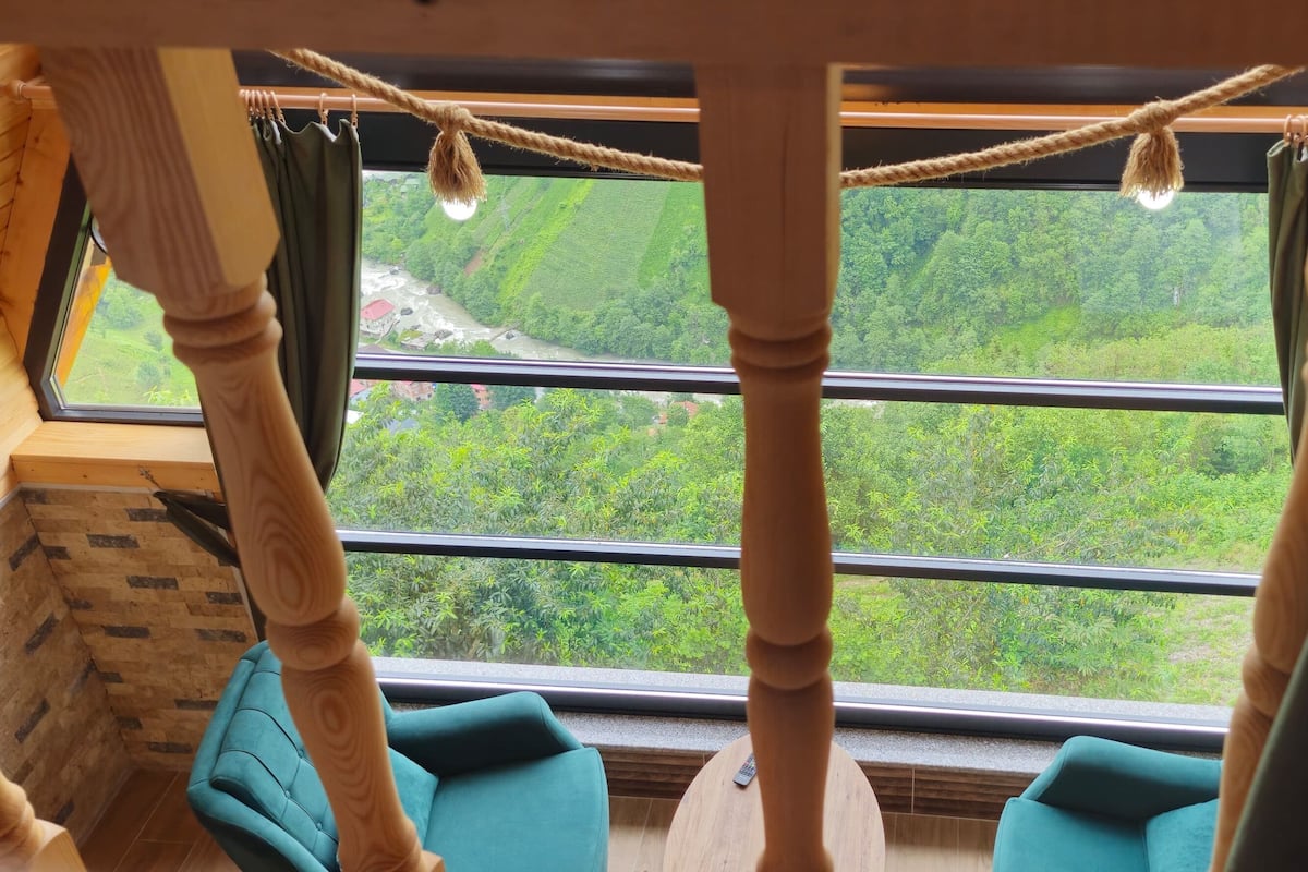 A room with a large window, wooden beams, and a green cushioned chair.