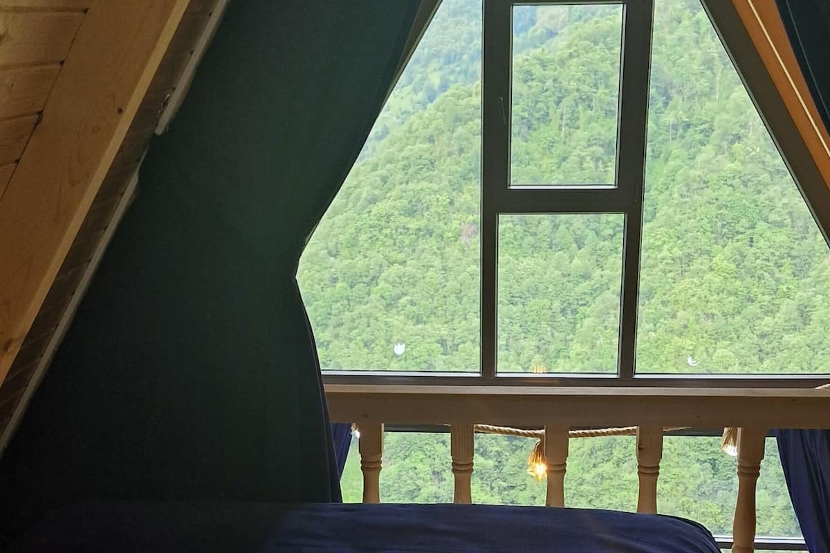A bedroom with a bed, pillows, and a view of a green landscape through a window.