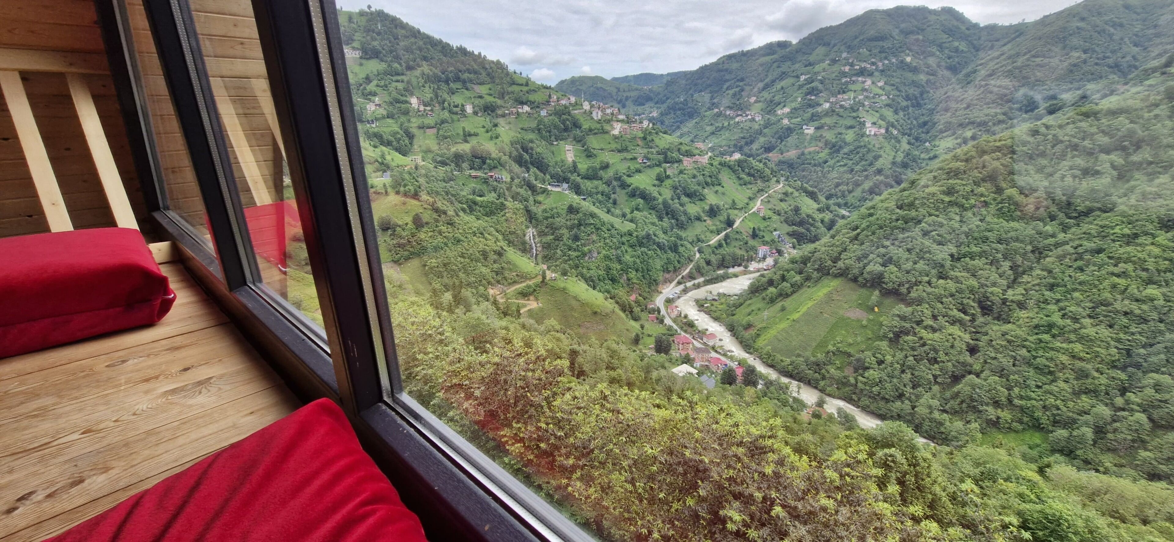 Una habitación con un amplio ventanal que da a un valle con un río y casas dispersas.