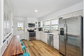 A modern kitchen with white cabinets, stainless steel appliances, and a wooden dining table. - Unobstructed views of the Santa Rosa Sound! Sleeps 12. (Navarre)