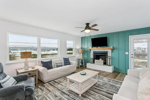 A living room with a fireplace, a ceiling fan, and large windows overlooking a beach. - Unobstructed views of the Santa Rosa Sound! Sleeps 12. (Navarre)