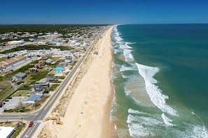 Ein Luftbild einer Küstenstadt mit einem langen Strand, Häusern und einer Straße parallel zur Küste.
