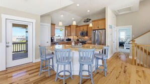 A spacious kitchen with a central island, wooden cabinets, stainless steel appliances, and a balcony. - High Tide Hideaway | Lux Ocean View in Kitty Hawk (Kitty Hawk)
