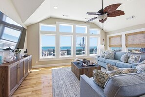 Ein geräumiges Wohnzimmer mit großem Fenster zum Meer, einem Deckenventilator und einer gemütlichen Sitzecke.