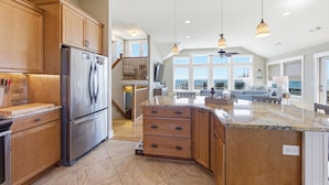 A spacious kitchen with a large island, wooden cabinets, and a stainless steel refrigerator. - High Tide Hideaway | Lux Ocean View in Kitty Hawk (Kitty Hawk)