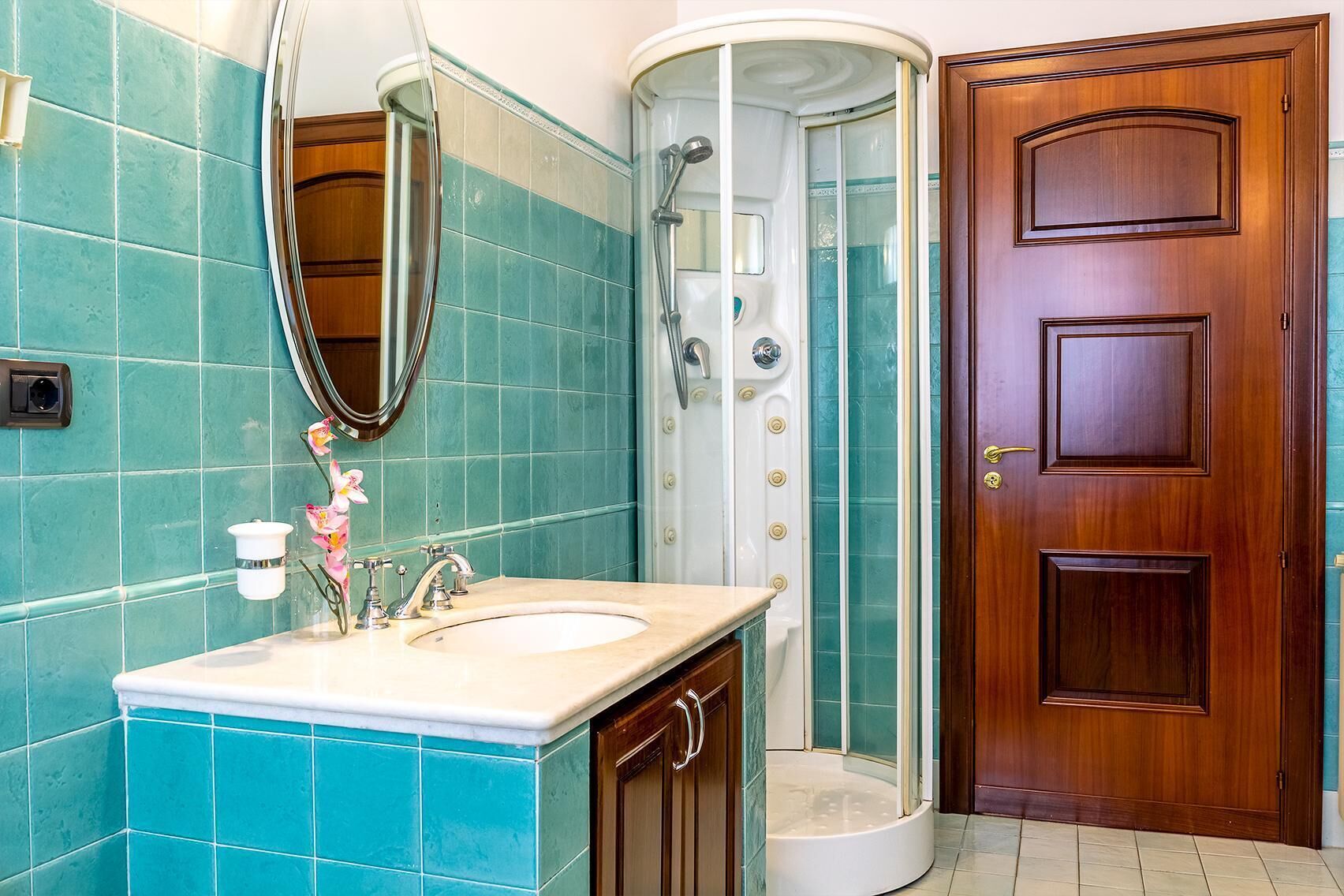 A bathroom with a sink, mirror, shower, and a wooden door.