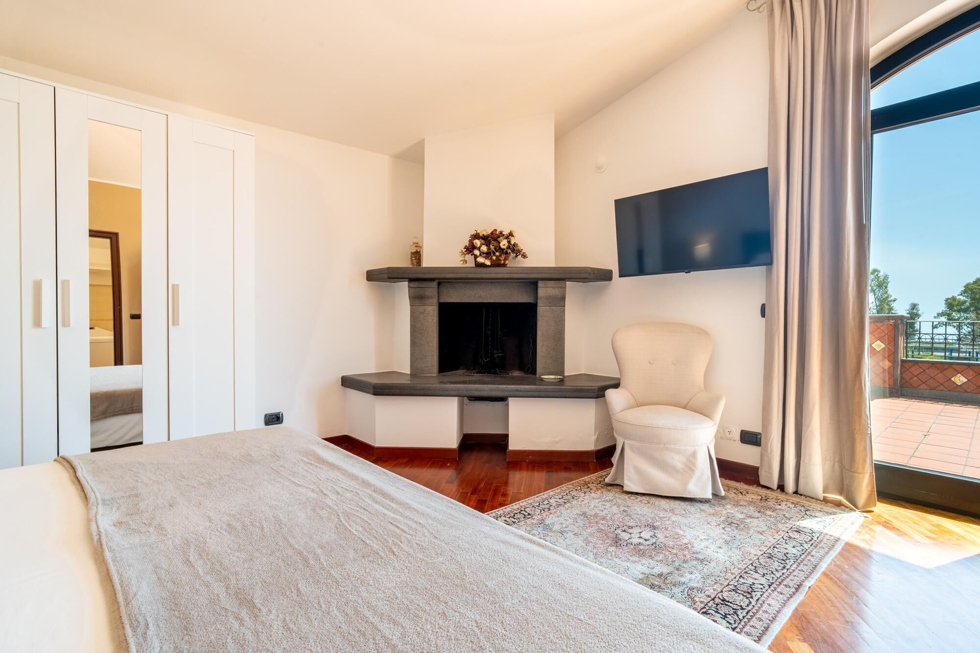 A bedroom with a bed, a fireplace, a chair, and a TV.