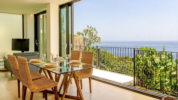 A dining area with a glass table and wicker chairs, a flat-screen TV, and a view of the sea. - Suite Onda Reale - Acireale (Acireale)
