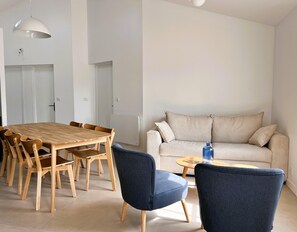 Ein modernes Wohnzimmer mit einem Holzes Esstisch, blauen Stühlen, einem beigen Sofa und einem kleinen runden Couchtisch.