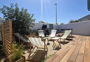 Eine Holzterrasse mit Sitzgelegenheiten, einem Grill und einer Pergola.
