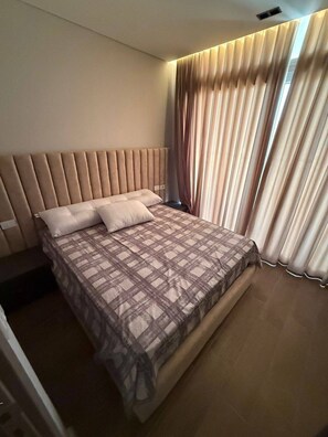 Un dormitorio moderno con una cama grande, cabecera y una ventana con cortinas.