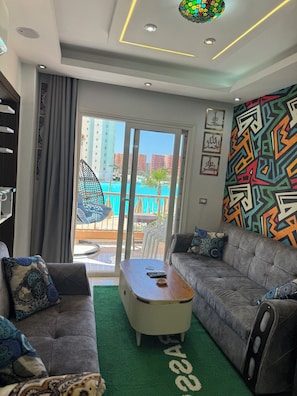 Un salon moderne avec un canapé, une table basse et une vue sur une piscine et des immeubles.