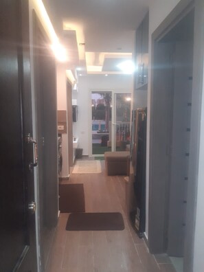 A hallway with a door on the left, a bench on the right, and a view of a pool and outdoor area through a glass door.