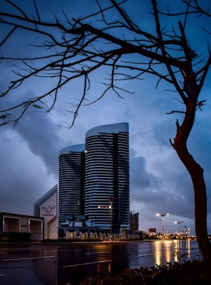 Un bâtiment moderne à la façade incurvée, doté d’un parking et bordé d’une étendue d’eau au premier plan.