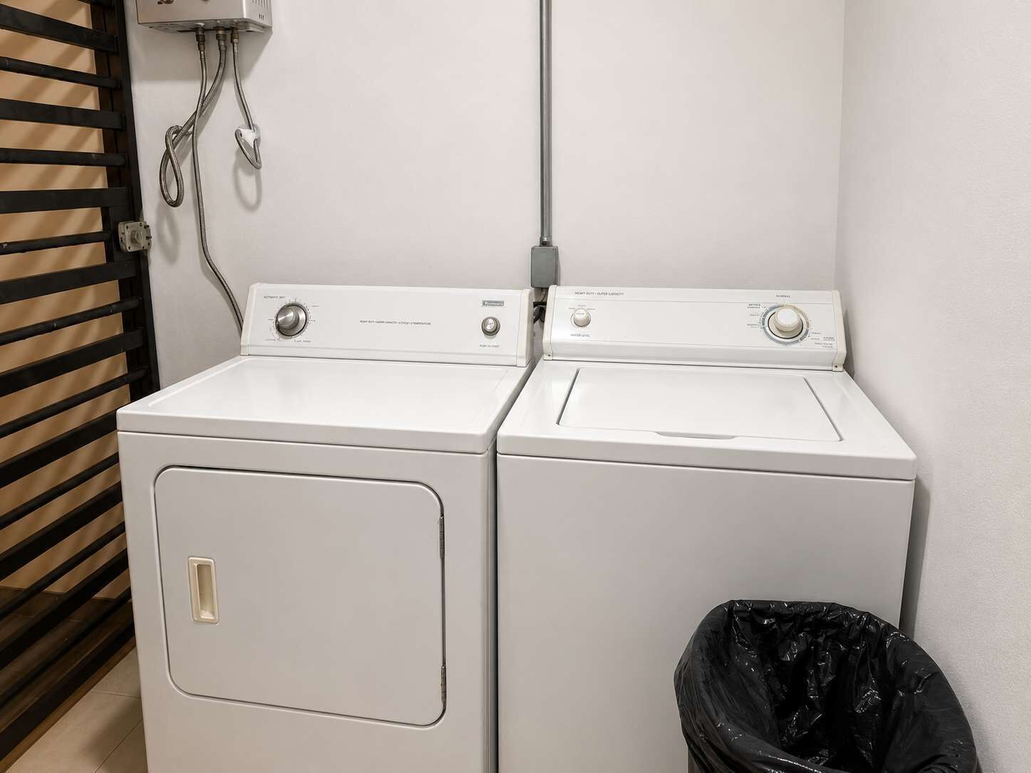 Un espace buanderie comprenant deux machines à laver à chargement frontal blanches et une poubelle noire.