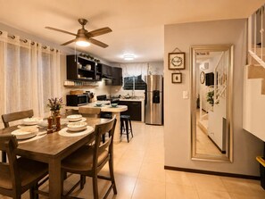 A modern kitchen with a dining area, featuring a ceiling fan, stainless steel appliances, and a dining table set for four.