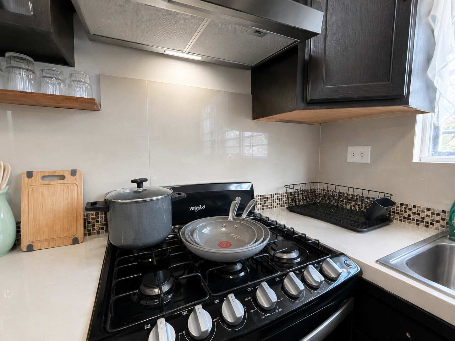 A modern kitchen with a gas stove, a pot on the burner, a cutting board, and a metal rack.