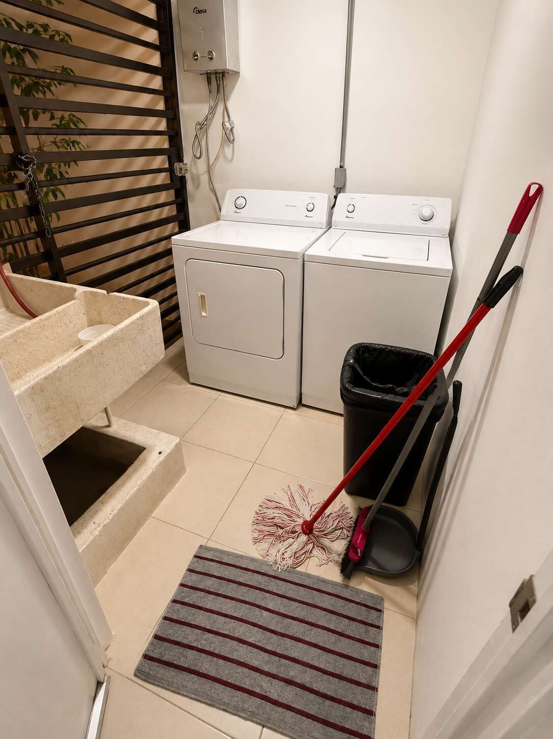 A laundry area with two washing machines, a trash bin, and a mop.