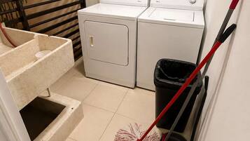 A laundry area with two washing machines, a trash bin, and a mop.