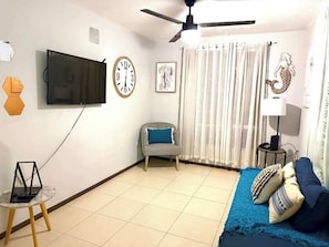A living room with a flat-screen TV, a chair, a sofa, a lamp, and a curtain.