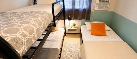 A room with two beds, a small table with a lamp, a potted plant, and a wall sign.