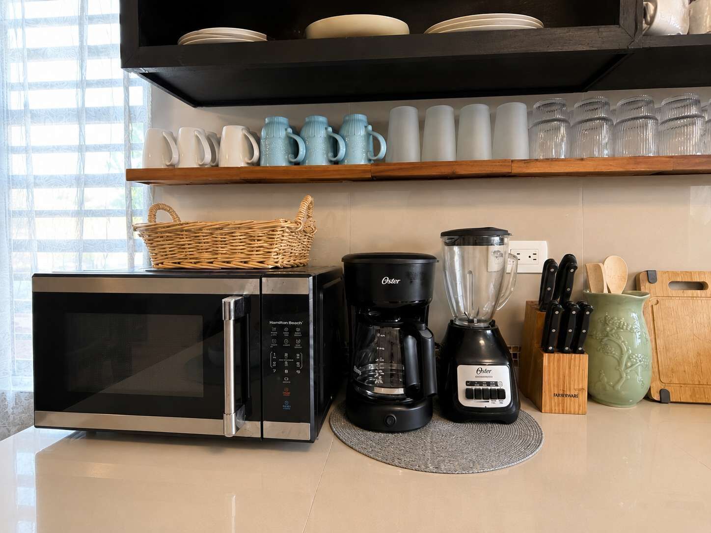 A kitchen with a microwave, coffee maker, blender, and a basket on the counter.