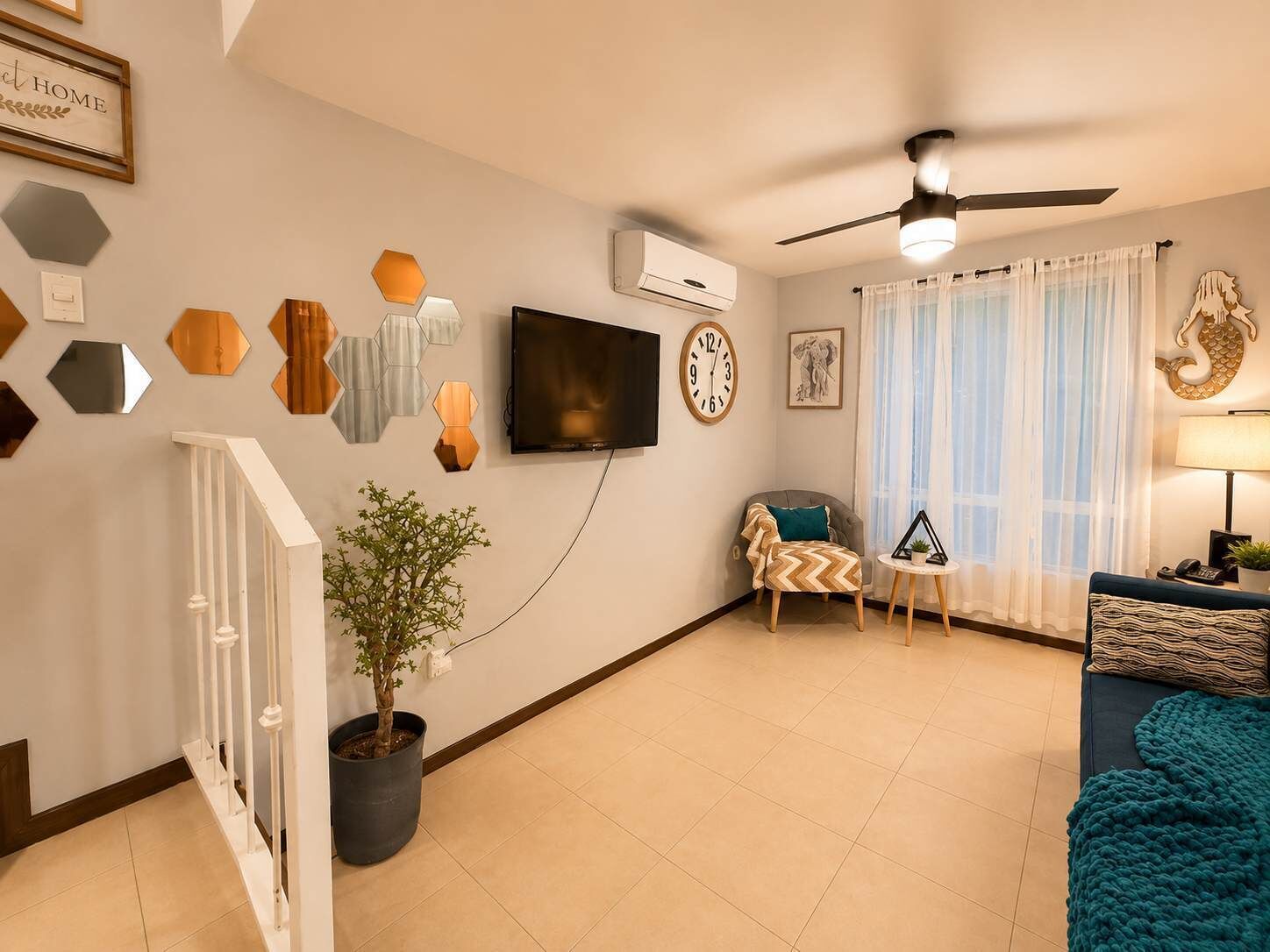 A living room with a TV, a clock, a plant, a sofa, and a ceiling fan.