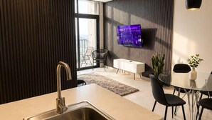 A modern kitchen with a built-in sink, a dining area with a glass table, and a flat-screen TV mounted on the wall. - Maravilloso Apt 7px Frente arena Mty (Monterrey)