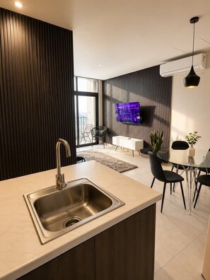 Una cocina moderna con un lavamanos integrado, un comedor con mesa de vidrio y un televisor de pantalla plana montado en la pared.
